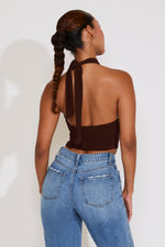 Woman wearing a brown halter top with a ribbon and blue jeans on a white background