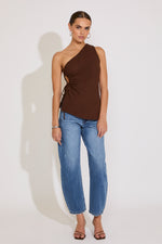 Woman wearing a brown one-shoulder top and blue jeans against a white background
