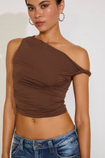 Woman wearing a brown one-shoulder top and blue jeans on a white background