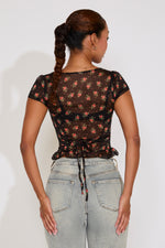 Woman wearing a black floral top and light blue jeans against a white background