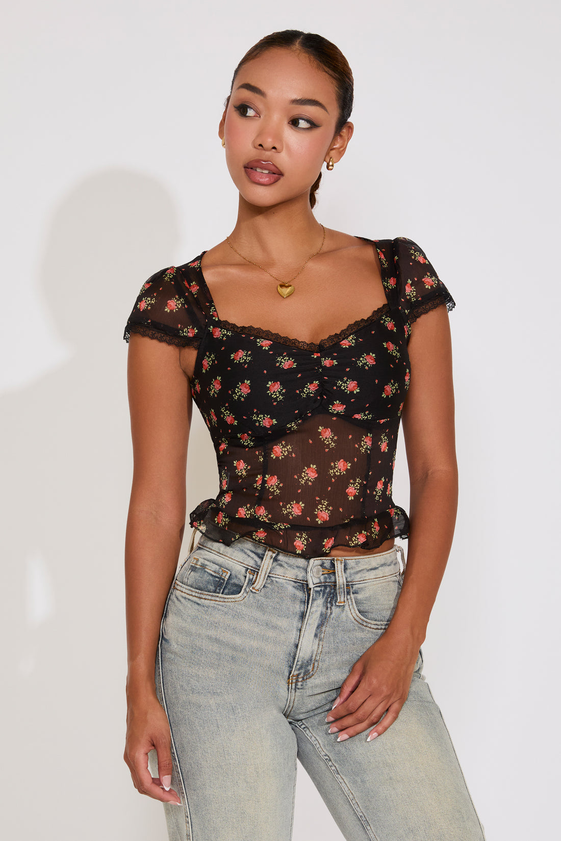 Woman wearing a black floral top and light blue jeans against a white background