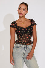 Woman wearing a black floral top and light blue jeans against a white background