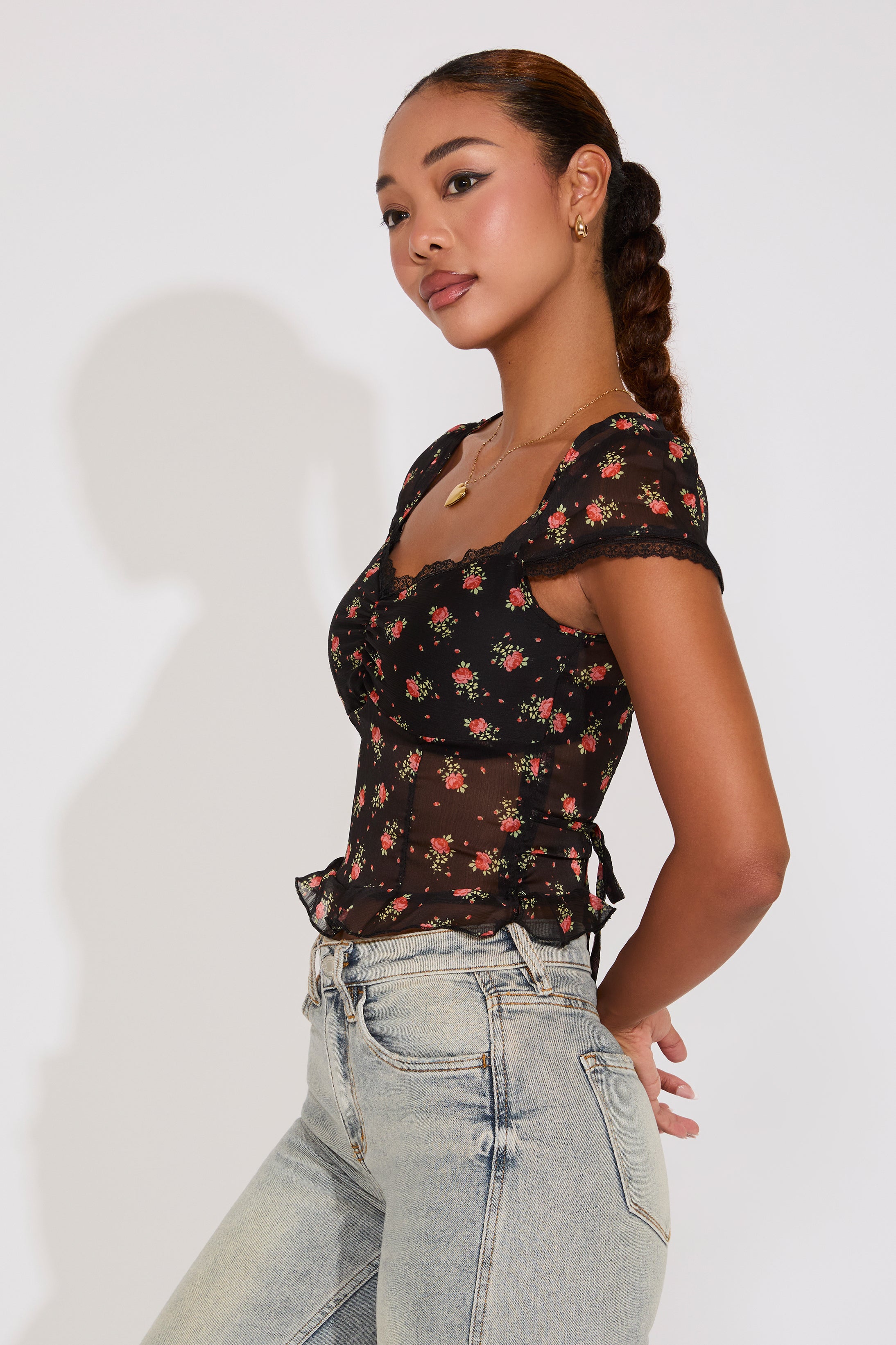 Woman wearing a black floral top and light blue jeans against a white background