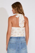 Woman wearing a white floral halter top and blue denim skirt on a plain background