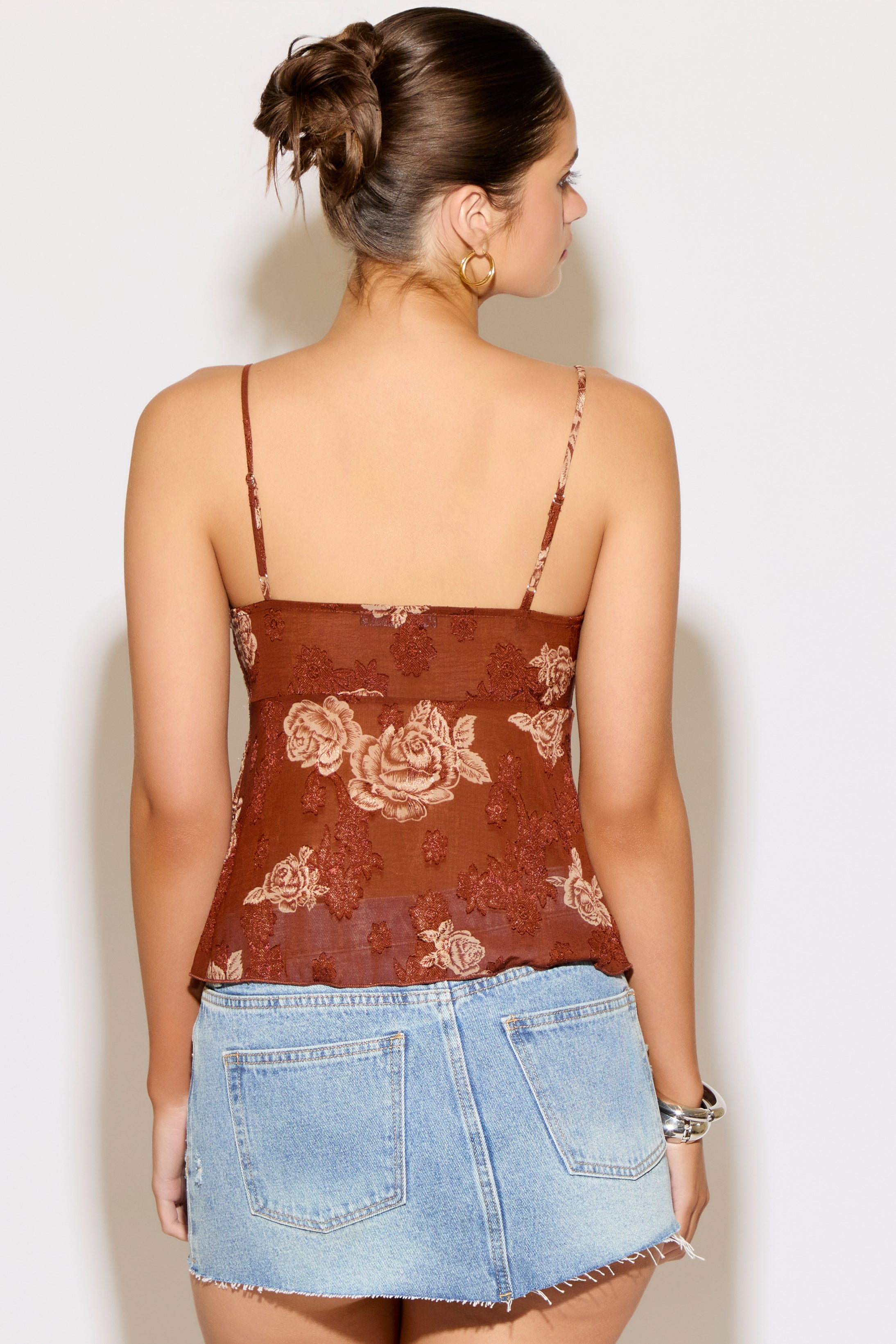 Woman wearing a brown floral top and denim skirt against a white background