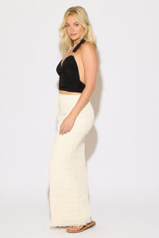 Model is wearing a black open back tie neck ruched top with metal detail with a cream maxi skirt on a white background.