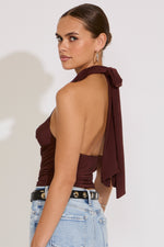Woman wearing a brown halter top with a bow detail on a white background