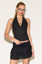 Woman wearing a black halter top with white polka dots and a black skirt on a white background