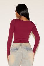 Person wearing a burgundy long-sleeve top and light blue jeans against a white background