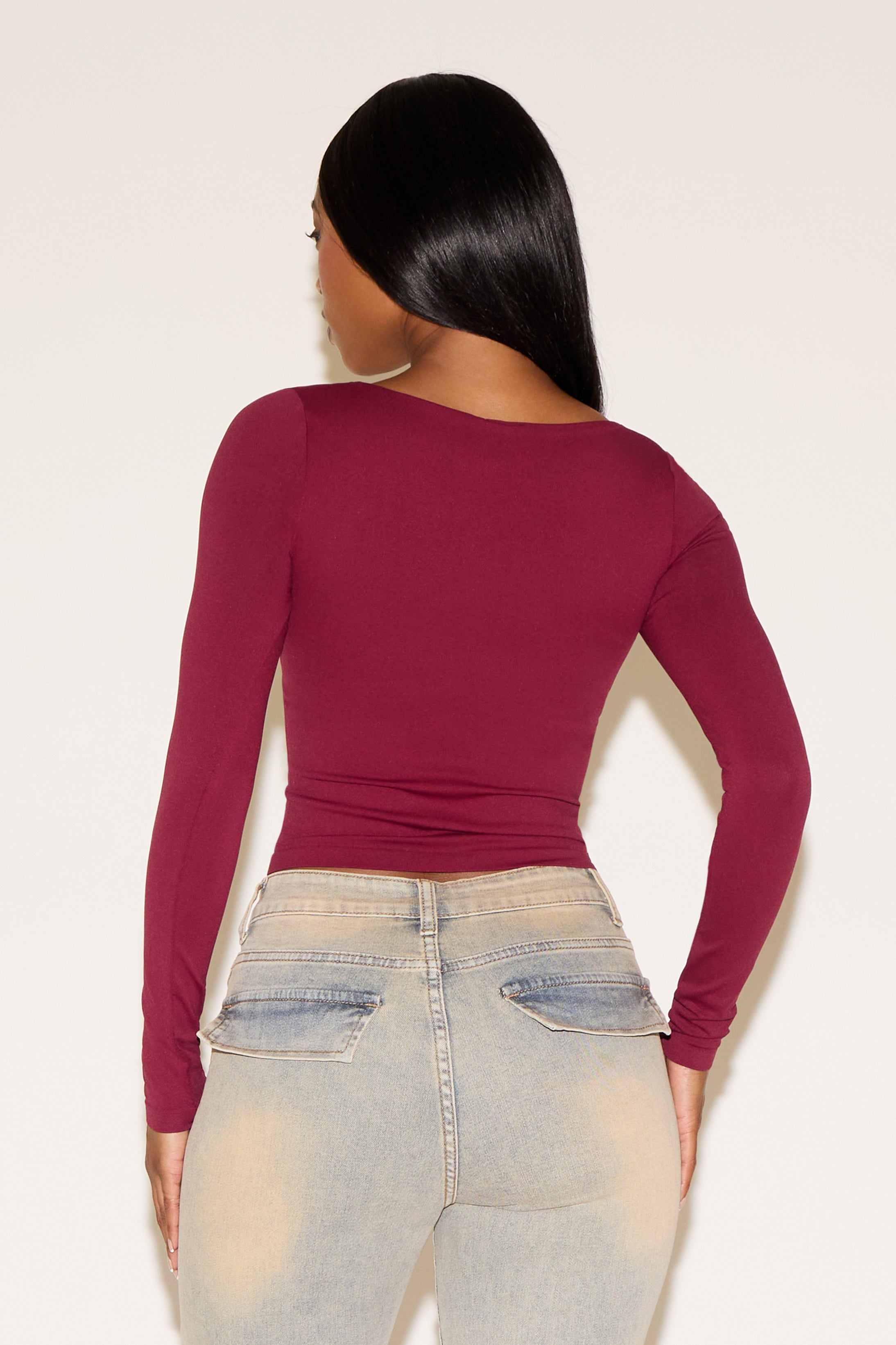Person wearing a burgundy long-sleeve top and light blue jeans against a white background