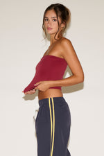 Woman wearing a strapless burgundy top and navy pants with yellow stripes against a white background