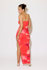 Woman wearing a strapless, colorful dress with a high slit on a white background