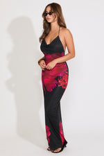 Model is wearing a black large rose print mesh tie neck maxi dress paired with some sunglasses on a white background.