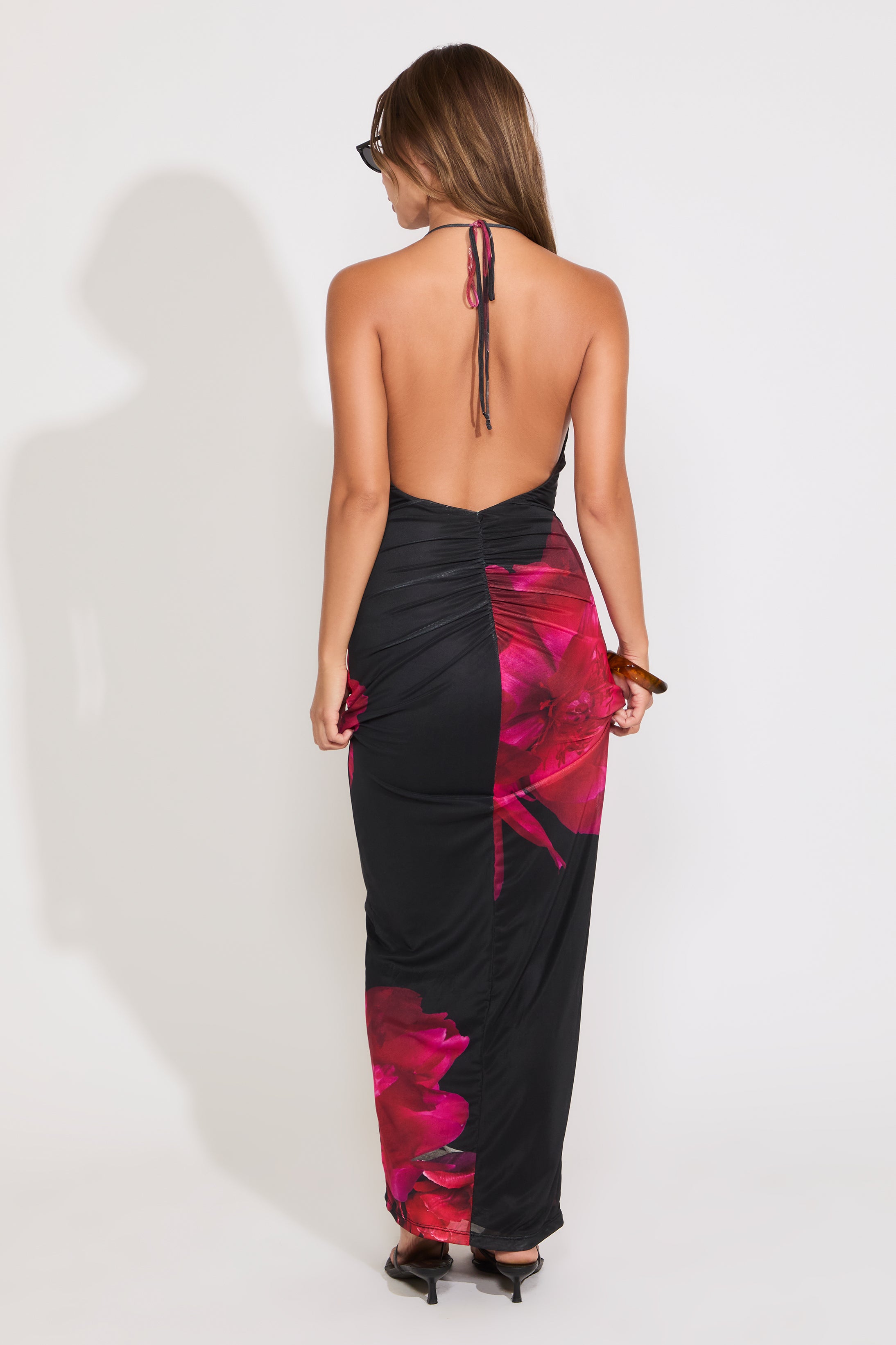 Model is wearing a black large rose print mesh tie neck maxi dress paired with some sunglasses on a white background.