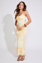 Model is wearing yellow FLORAL BACK CLOSURE MERMAID SLEEVELESS MAXI DRESS with black heels on a white background.