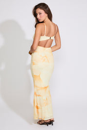 Model is wearing yellow FLORAL BACK CLOSURE MERMAID SLEEVELESS MAXI DRESS with black heels on a white background.