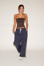 Woman wearing a brown strapless top and navy pants with a yellow stripe on a white background