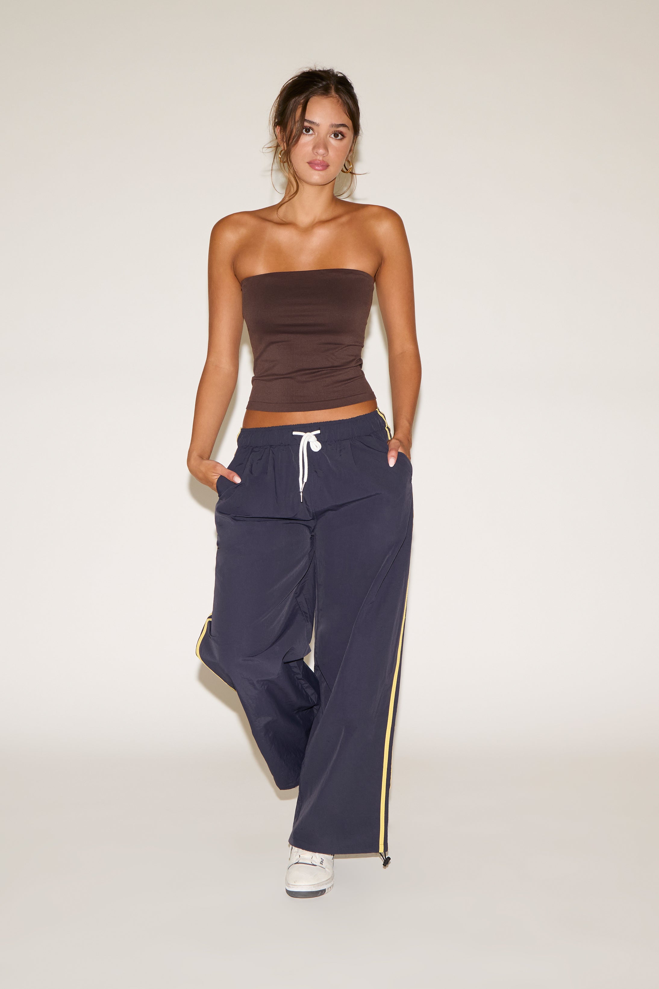 Woman wearing a brown strapless top and navy pants with a yellow stripe on a white background