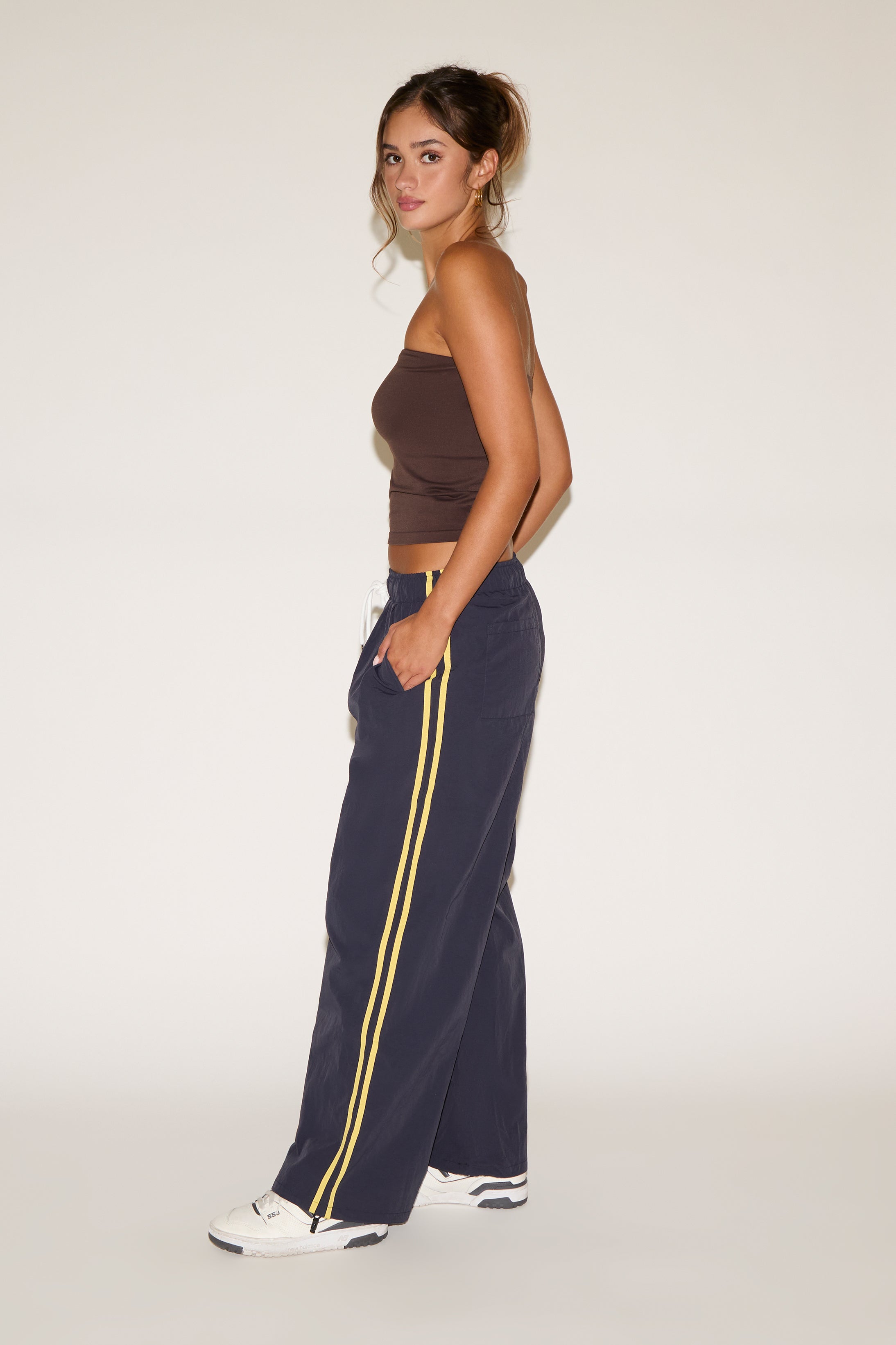 Woman wearing a brown top and navy pants with yellow stripes on a white background