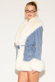 Person wearing a white fur coat with denim accents on a plain background