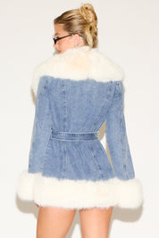 Denim jacket with white fur trim worn by a person on a plain background