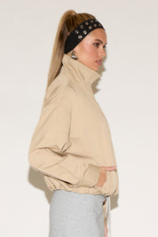 A woman models a beige zip-front jacket and a grey skirt against a white background.