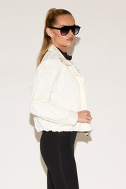 Woman wearing a white jacket and black sunglasses against a plain background