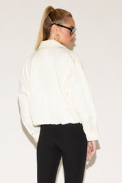 Person wearing a white jacket and black pants against a plain background