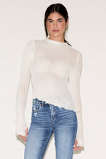 Woman wearing a white ribbed sweater and blue jeans against a plain background