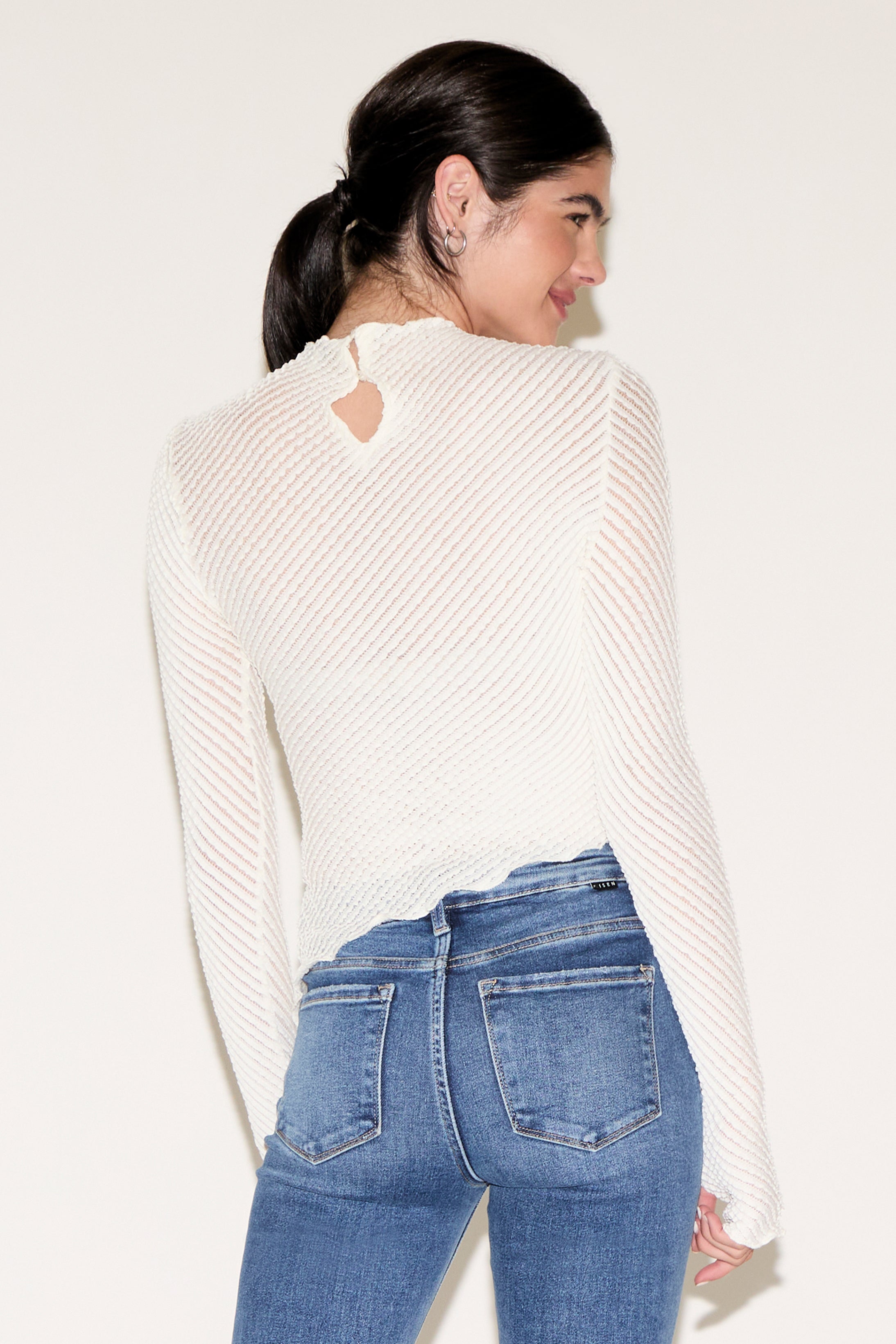 Person wearing a white ribbed sweater and blue jeans against a plain background