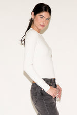 Woman wearing a white sweater and gray jeans against a plain background