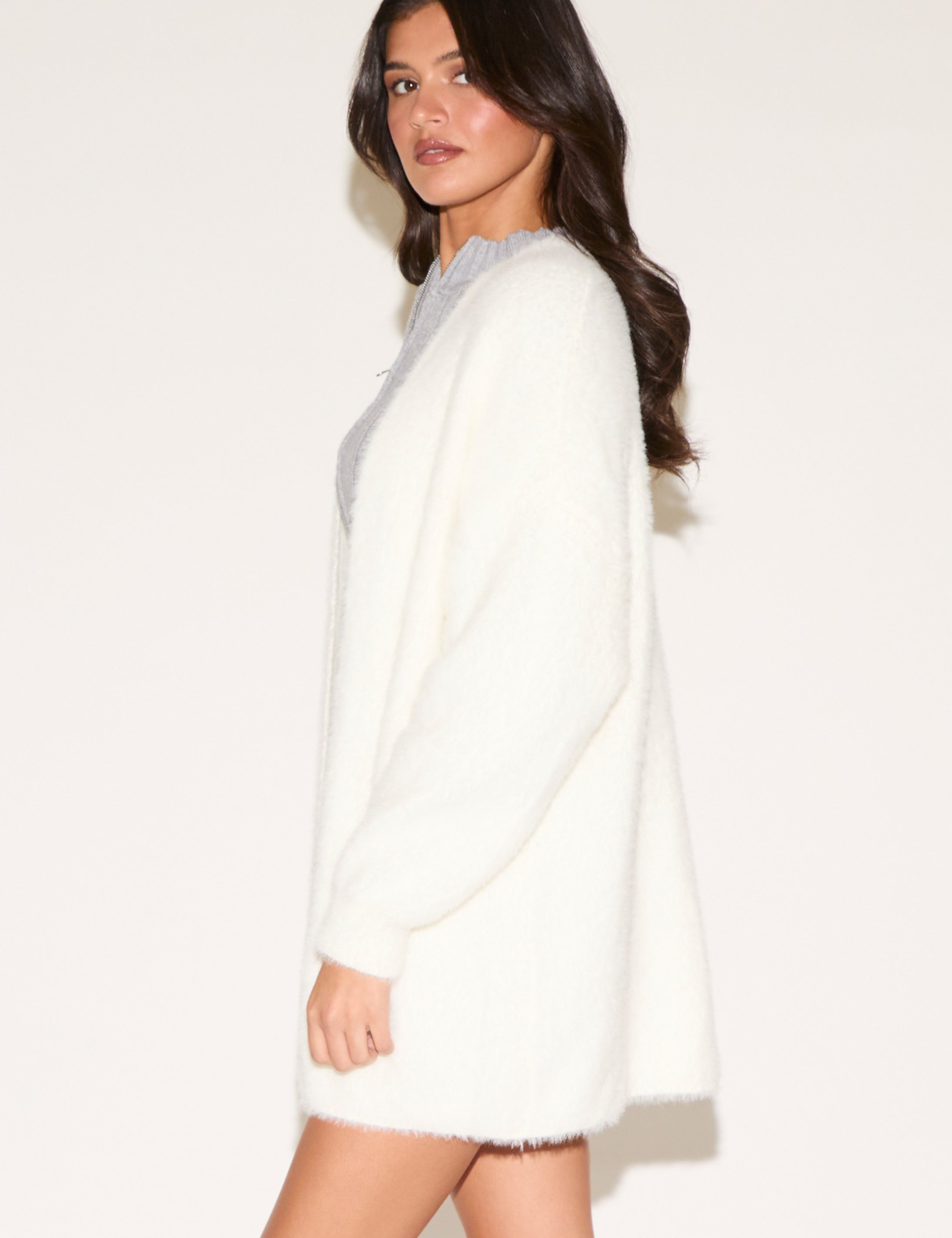 Woman wearing a white cardigan over a gray top on a plain background