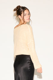 Woman wearing a beige sweater and black satin skirt against a white background