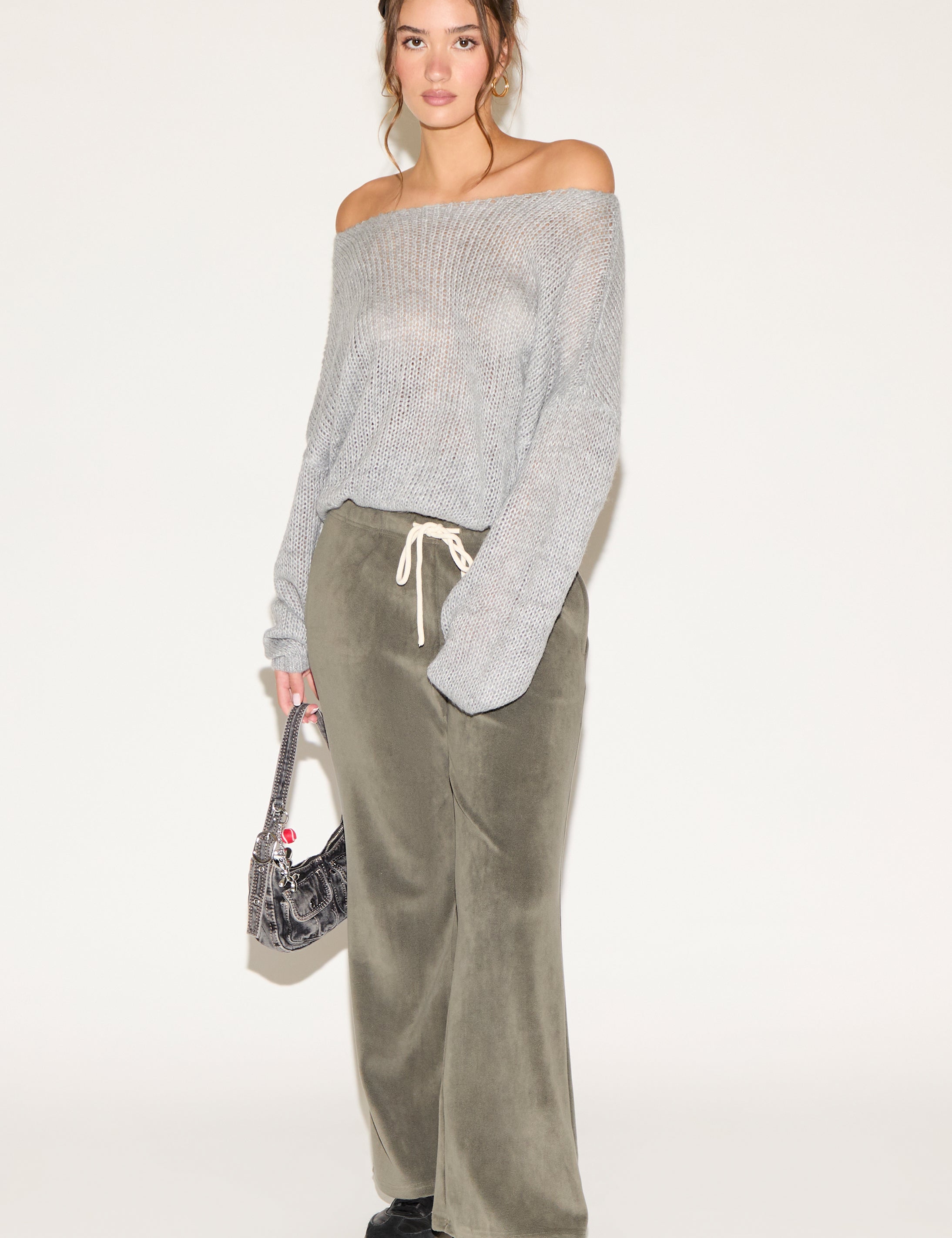 Woman wearing a gray off-shoulder sweater and green velvet pants on a white background