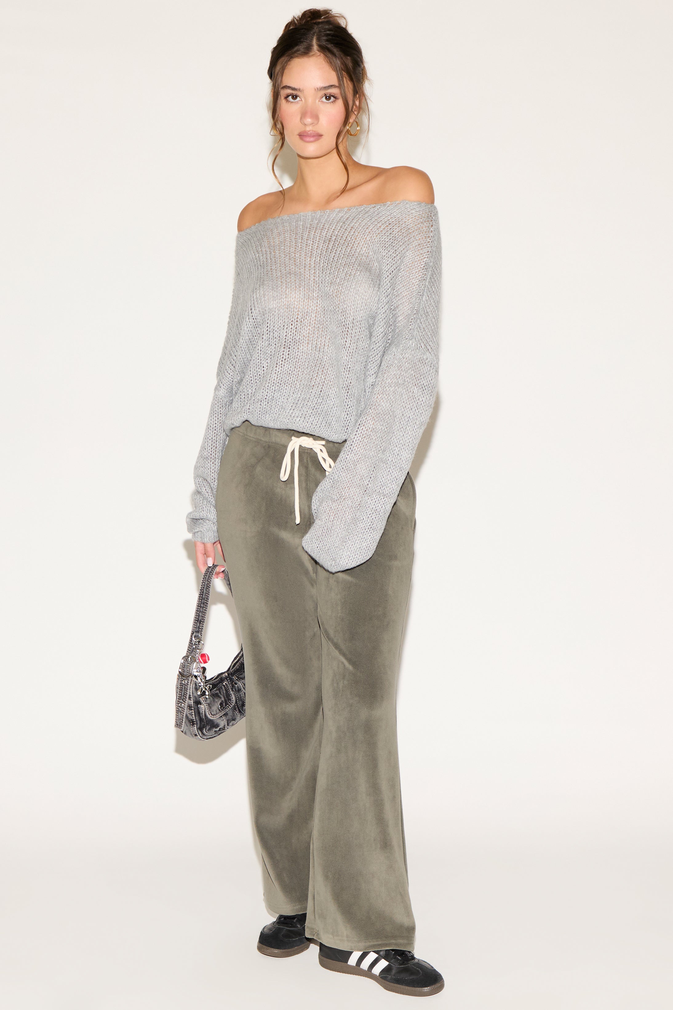 Woman wearing a gray off-shoulder sweater and green velvet pants on a white background