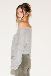 Woman wearing a light gray off-shoulder sweater and beige pants against a white background