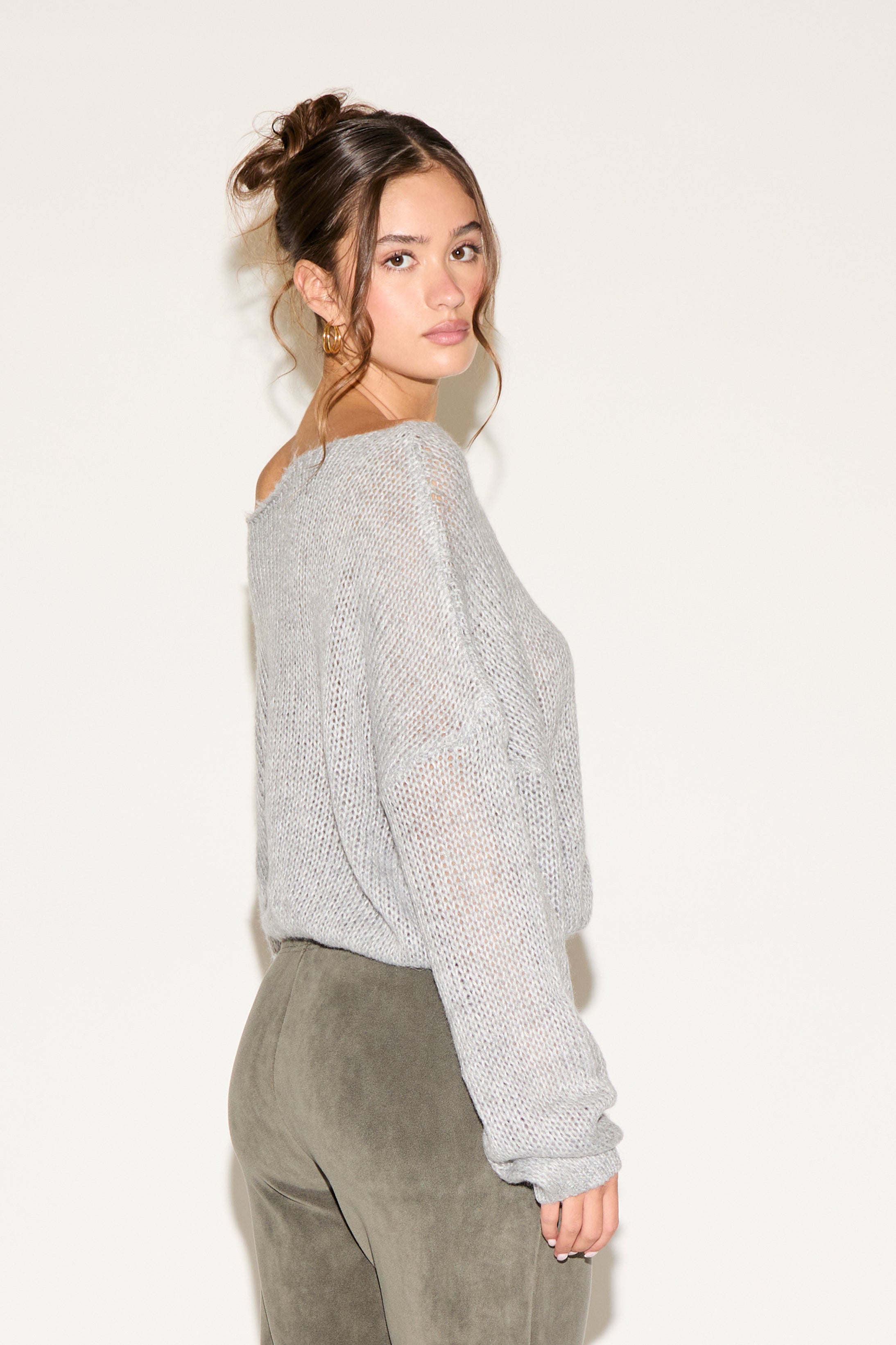 Woman wearing a light gray sweater and green pants on a plain background