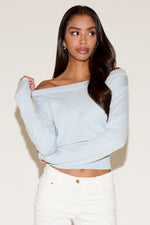 Woman wearing a light blue off-shoulder top and white pants against a plain background