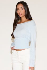 Woman wearing a light blue off-shoulder top and white pants on a beige background