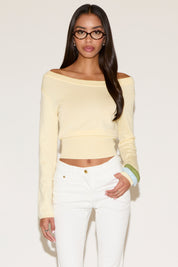 Woman wearing a light yellow long-sleeve top and white pants against a plain background
