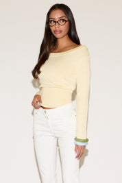 Woman wearing a light yellow long-sleeve top and white pants on a plain background