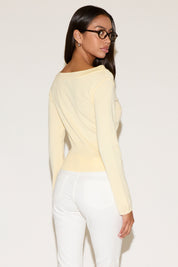 Woman wearing a light yellow long-sleeve top and white pants against a plain background