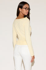 Woman wearing a light yellow long-sleeve top and white pants against a plain background