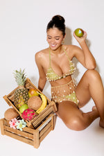 Woman in a bikini holding an apple next to a crate of fruits on a white background