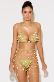 Woman wearing a green bikini top and beige netted skirt against a white background