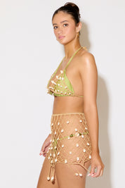 Woman wearing a green bikini top and beige netted skirt against a white background