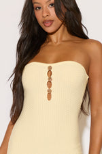 Woman wearing a strapless beige dress with decorative buttons on a white background