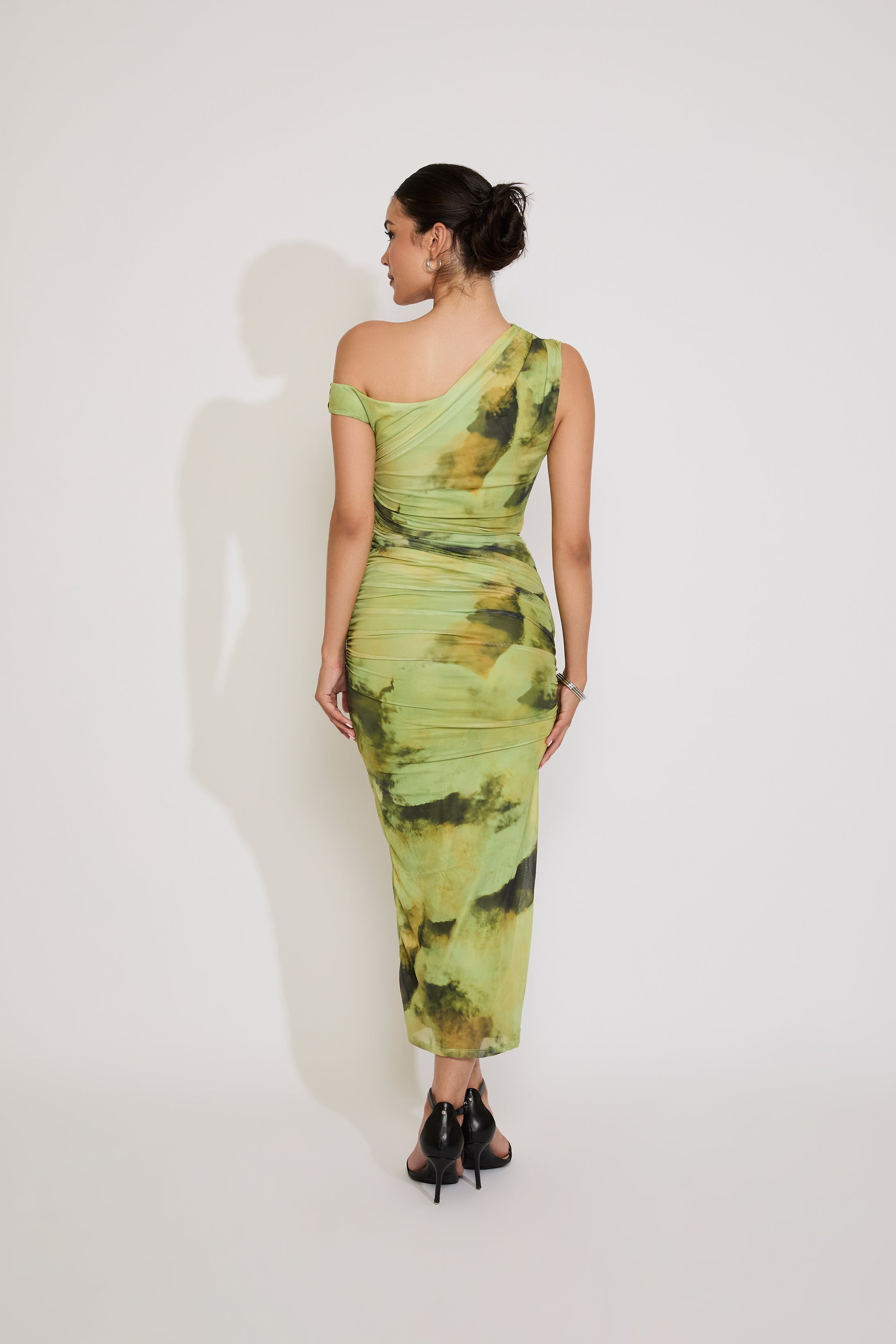 Woman wearing a green one-shoulder dress with abstract pattern on a white background