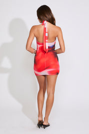 Model is wearing a red TIE DYE METAL DETAIL TIE NECK COWLED MINI DRESS with black heels on a white background.