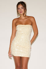 Woman wearing a strapless, light-colored sequin dress against a plain background
